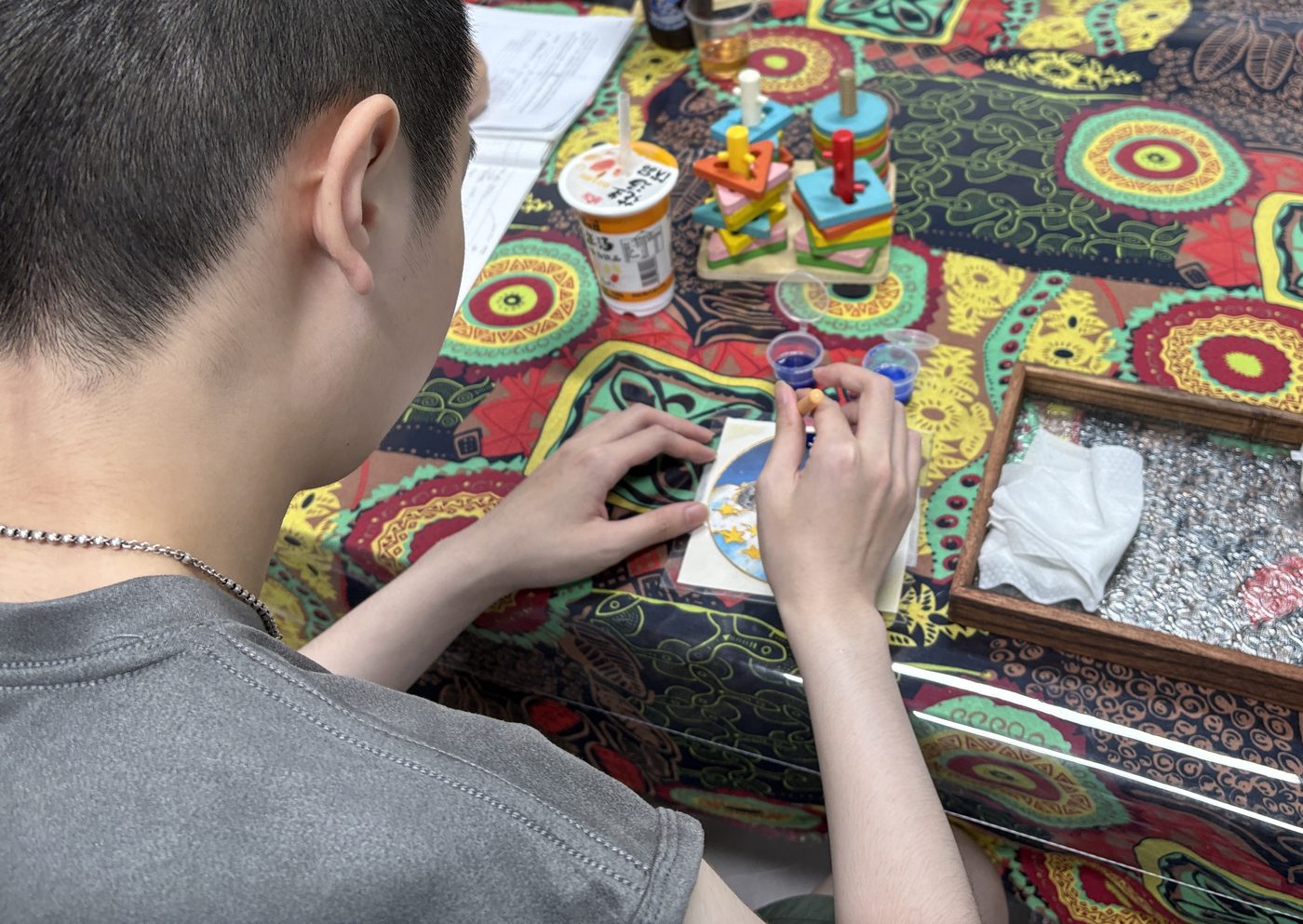 A member at the craft table painting a small hand-made piece, paint pots and tools laid out in front of him