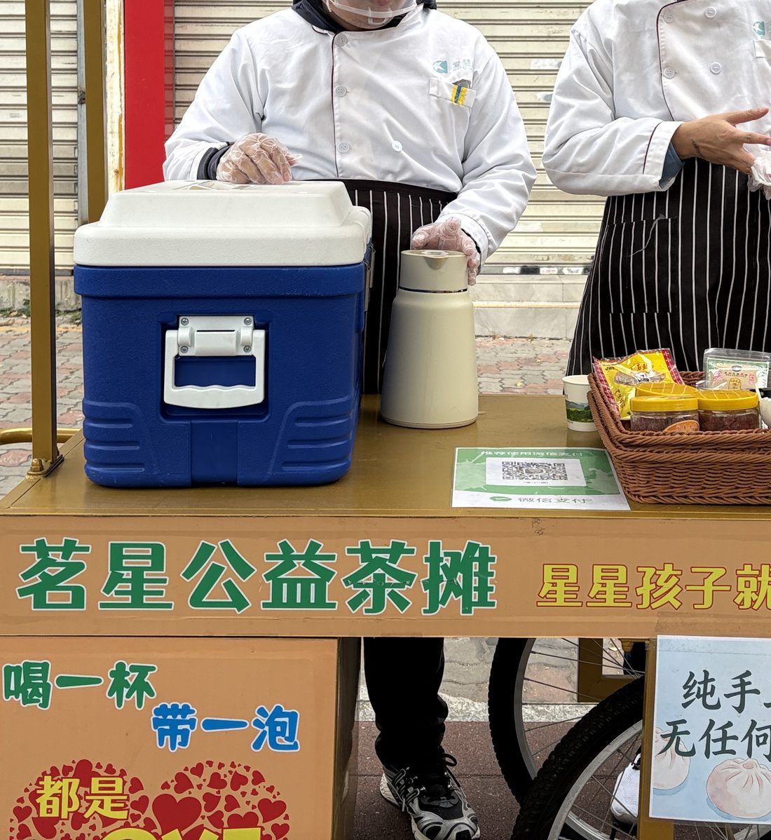 The Mingxing charity tea stall on a Xiamen street — a flask of brewed Tieguanyin and cups on the cart, with members in whites serving behind it