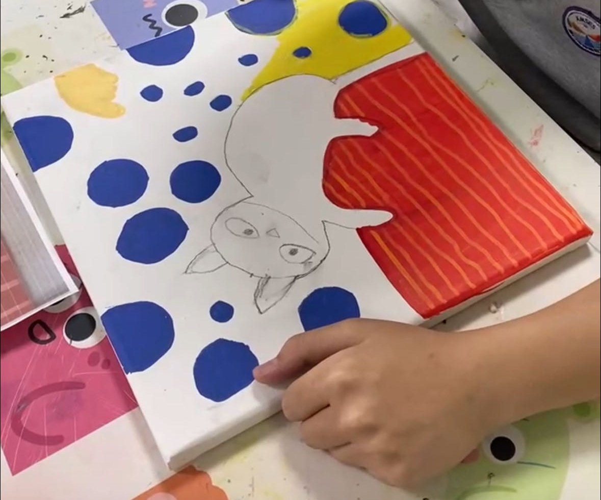 A hand steadying a canvas while drawing an animal in pencil among blue dots and red stripes