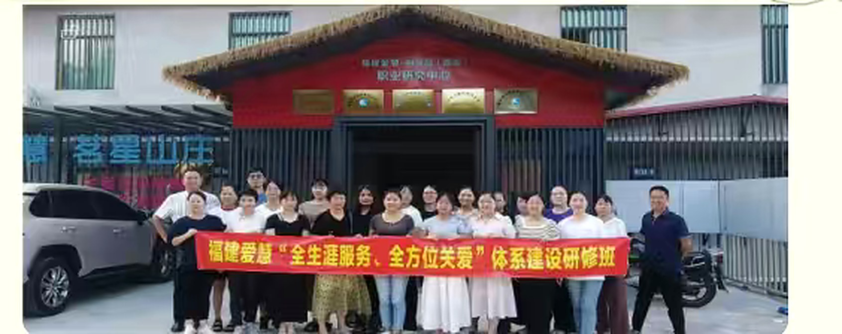 Staff, families and trainers standing across the front of the mountain lodge behind a red banner, under the plaques on the gable