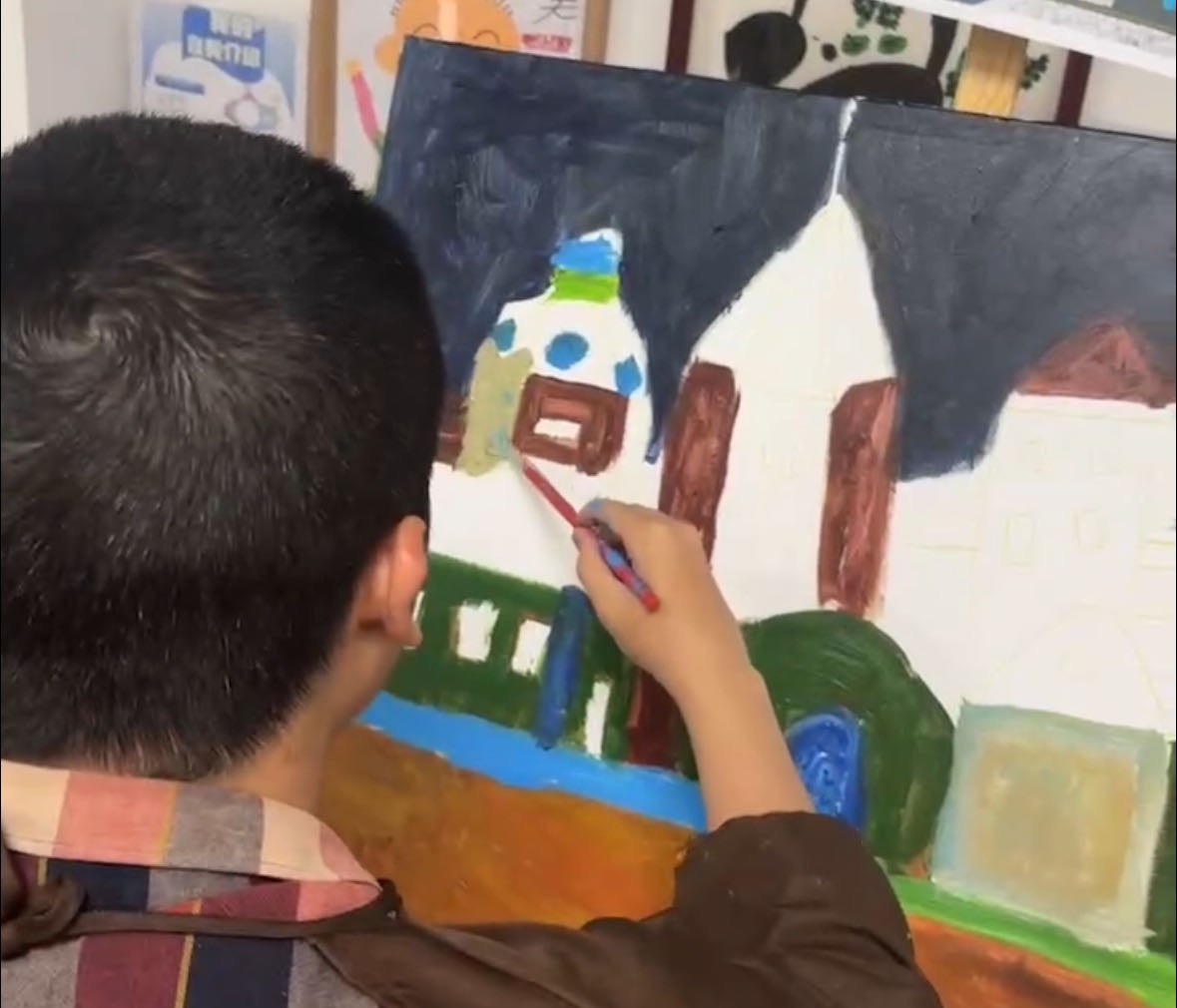 A member seen from behind, brush in hand, working on a large painting of a white house with a dark roof